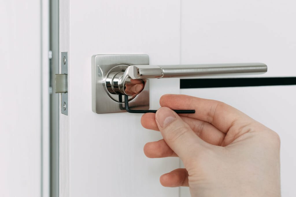 A locksmith is repairing an interior door lock. A locksmith Man fixing lock with L-Shaped Hex Wrench. Selective focus.