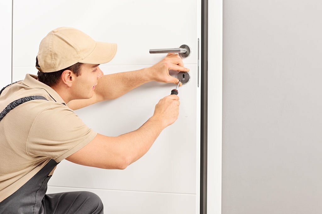 Young male locksmith installing a lock on a new door with a screwdriver