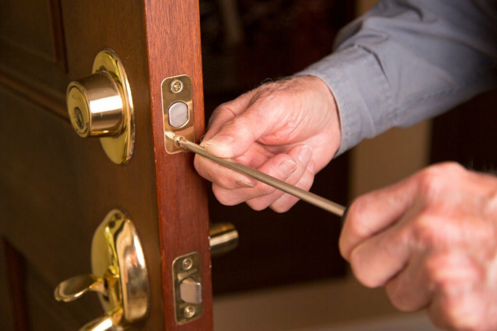 Locksmith or home owner installing or repairing new long on beautiful wood front door.  He wears blue uniform shirt.