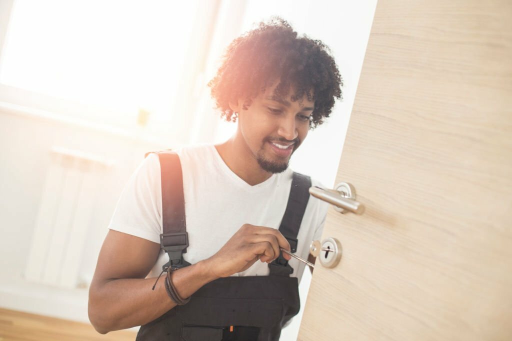 Young man fixing a lock on the door. About 25 years old, African male with curly hair.