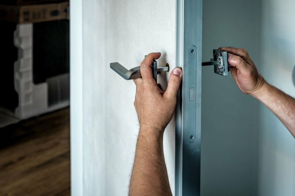 Locksmith repairing the doorknob. closeup of worker's hands installing new door locker. Industrial theme