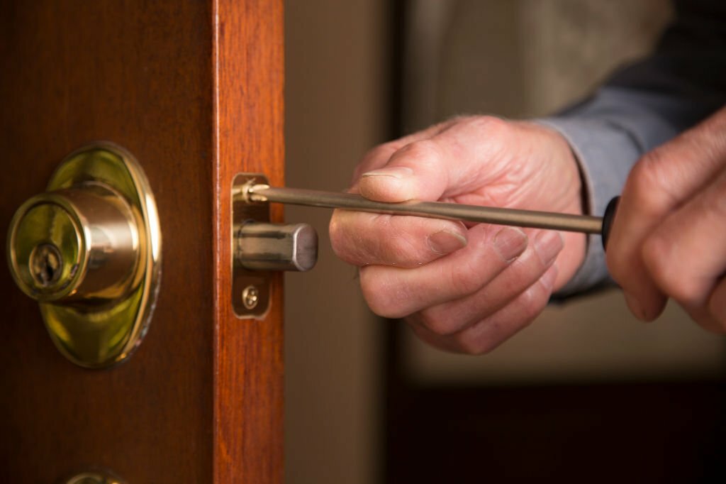 Worker in blue uniform or homeowner installing or repairing door knob on an interior door in the home.