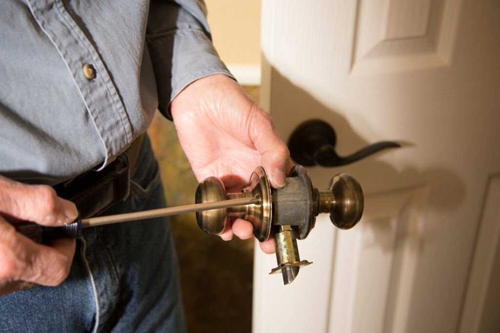 Worker in blue uniform or homeowner installing or repairing door knob on an interior door in the home.