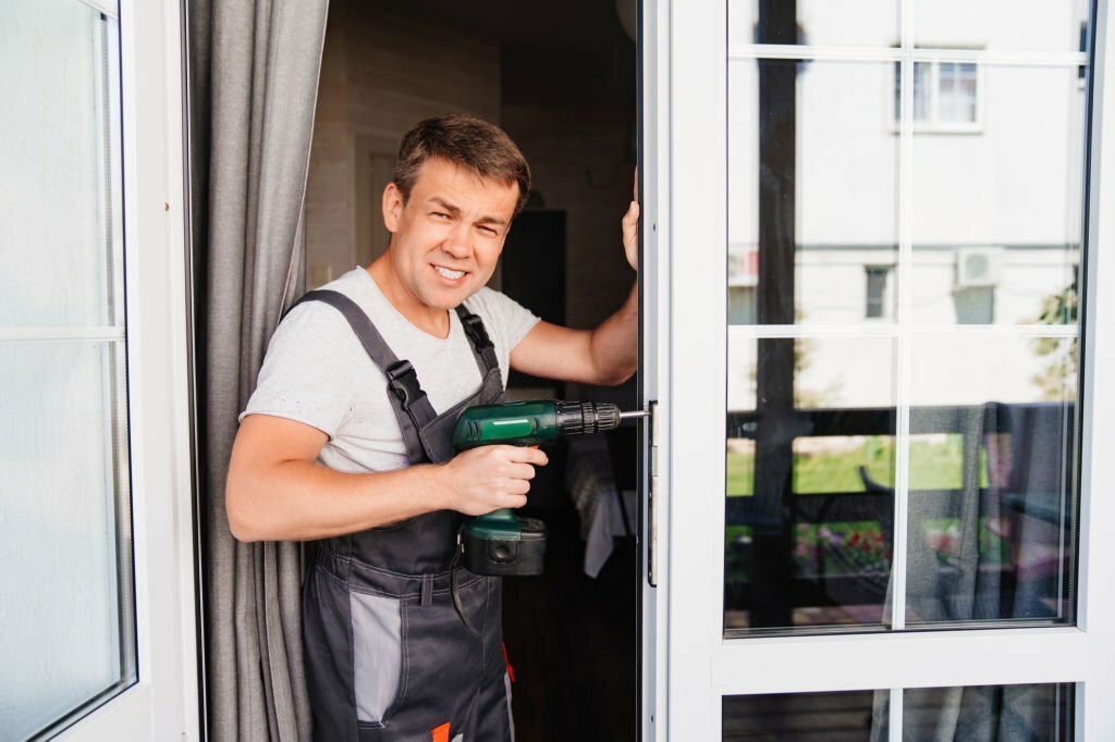A repairman repairs or adjusts window frames or glass doors on the terrace. services of a repairman or installer of furniture and doors.