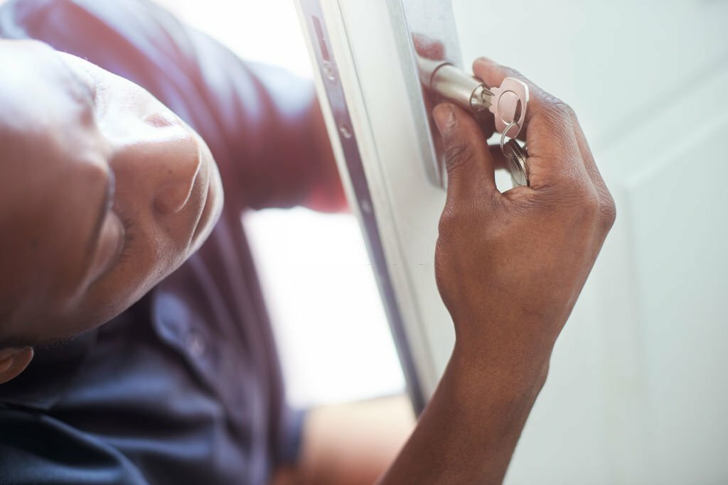 A young locksmith changing the lock on a residential front door.